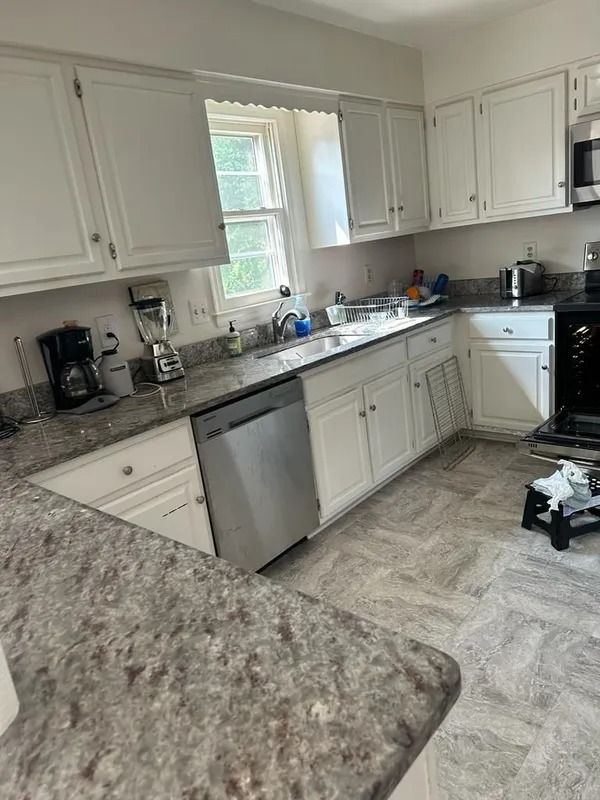 Bright white kitchen with granite countertops, white cabinets, and a dishwasher near a window.