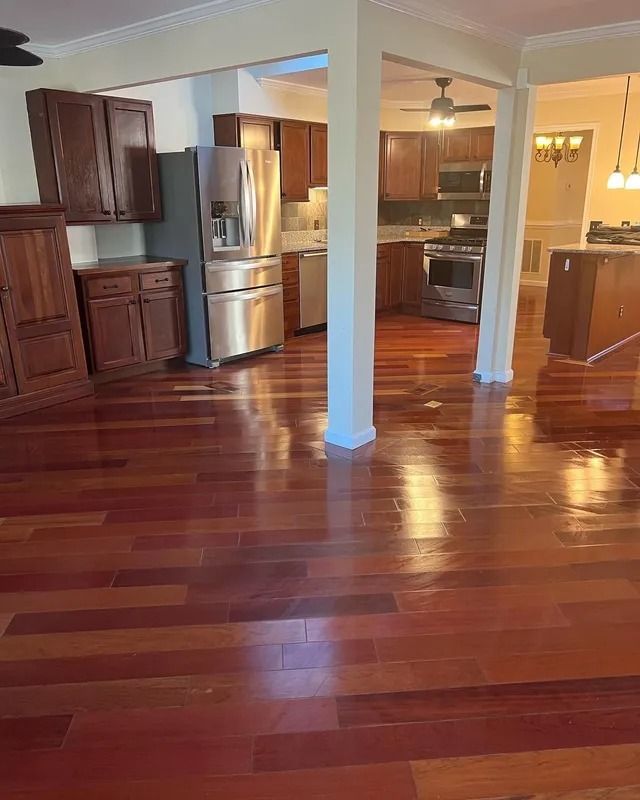 Empty kitchen and dining area with glossy hardwood floors, stainless fridge, and white support columns