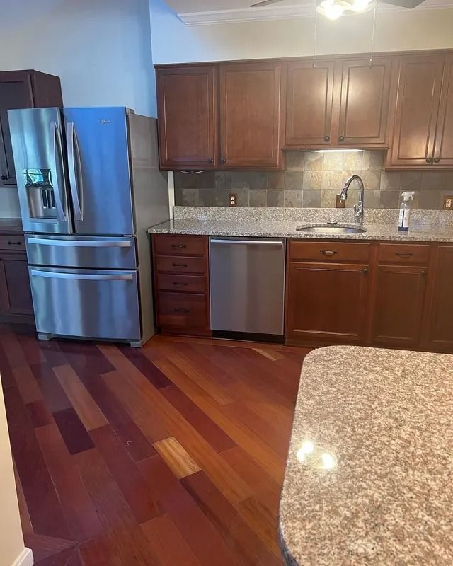 Modern kitchen with wood cabinets, stainless appliances, speckled counters, and hardwood floors