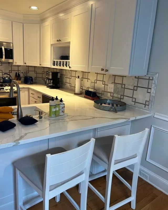 White kitchen with island, bar stools, and tiled backsplash under bright lighting