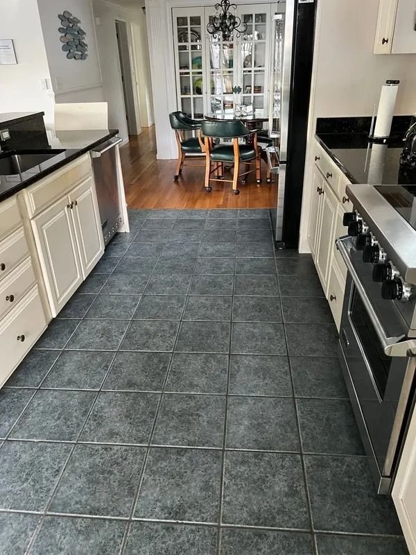 Modern kitchen with gray tile floor leading to a dining area and glass cabinet doors.