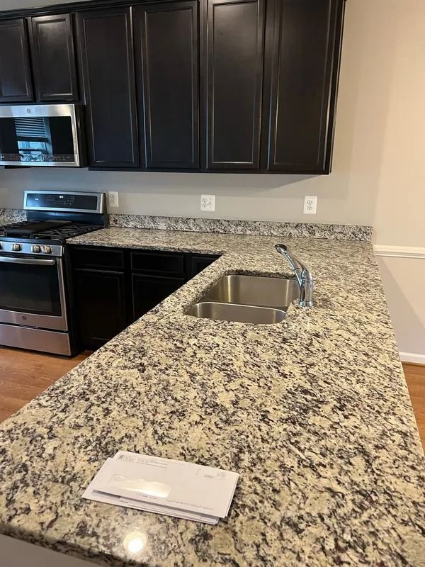Kitchen with granite countertop, stainless sink, black cabinets, and stove in the background