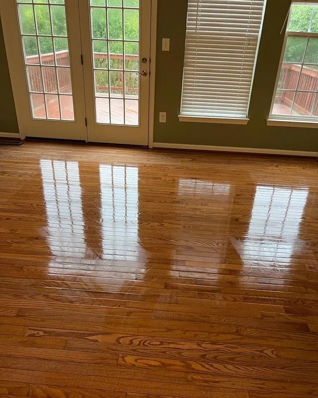 Empty room with shiny hardwood floor, French doors, and a window with blinds reflecting light.