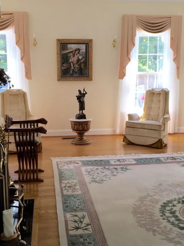 Elegant living room with twin windows, cream curtains, framed art, and a small statue on a pedestal