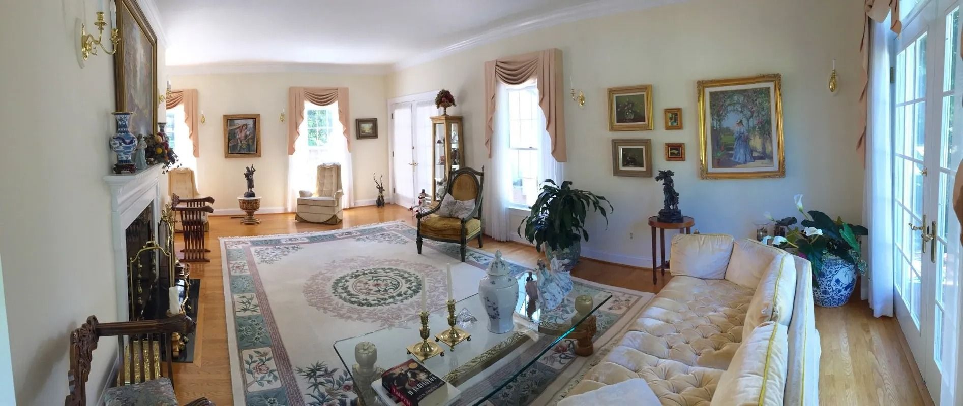 Bright living room with ornate sofas, framed art, and large windows around a central rug