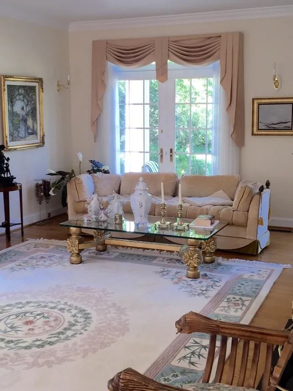 Elegant living room with cream sofa, glass coffee table, framed art, and large window with pink drapes