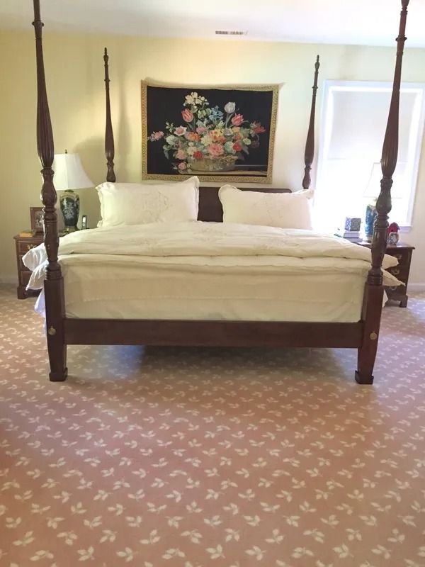 Spacious bedroom with a four-poster bed, white bedding, floral wall art, and patterned carpet