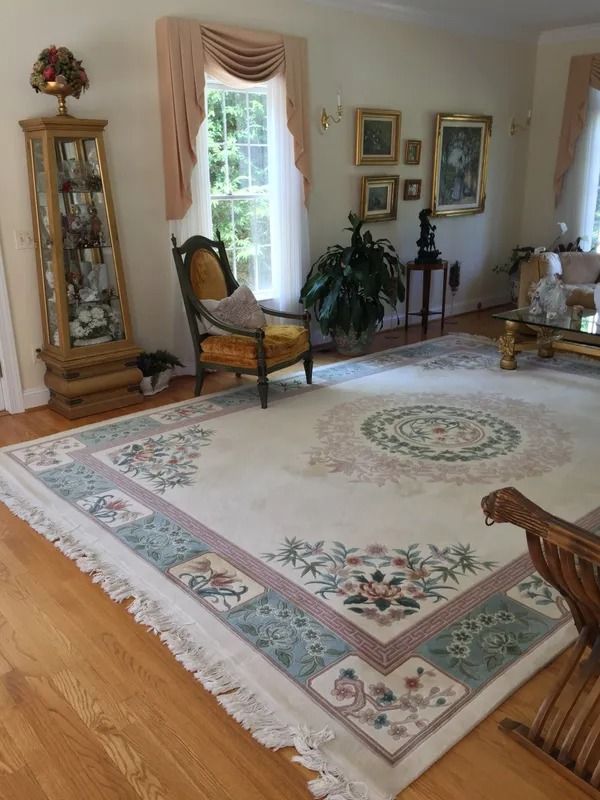 Elegant living room with floral area rug, wicker chair, glass cabinet, and framed wall art
