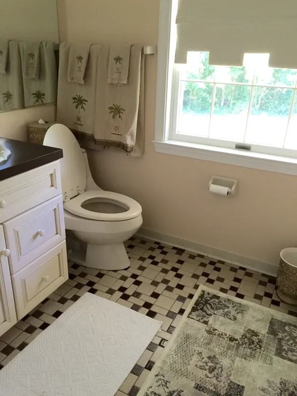Bathroom with toilet, vanity, patterned floor tile, towels, and a window letting in daylight.