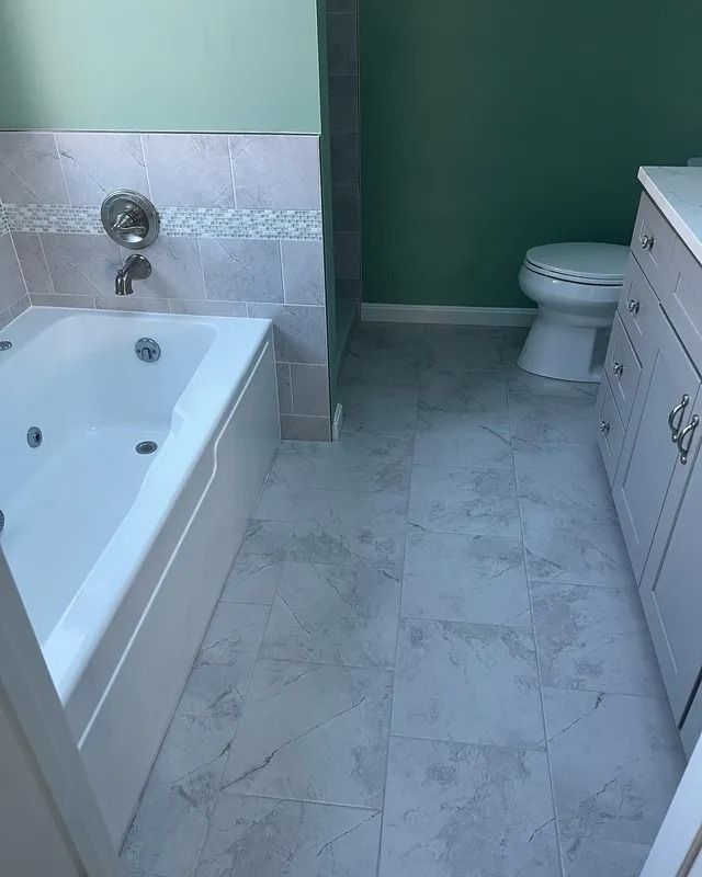 Bathroom with white tub, toilet, and vanity on light gray tile floor.