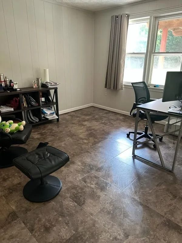 Small living room with desk, chair, shelving, window, and brown floor; black floor chair in foreground