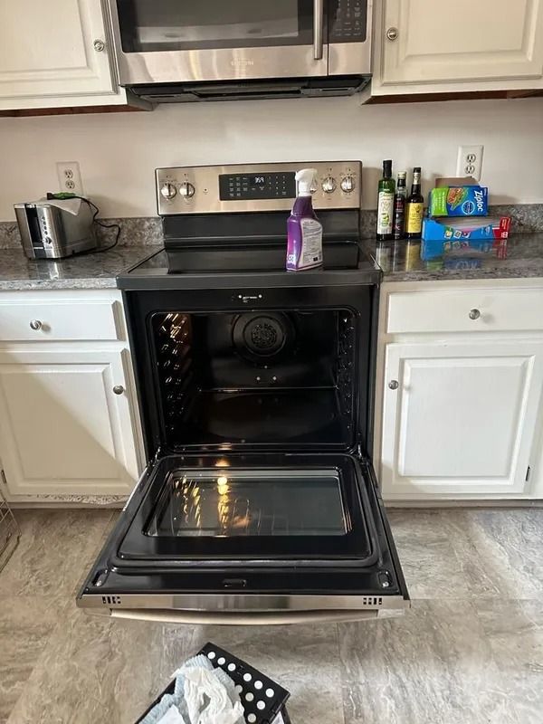 Open oven in a white kitchen with cleaning items on the stovetop and counters