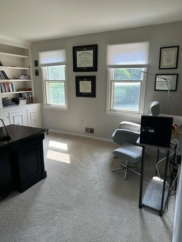 Bright home office with white walls, desk, chair, windows, and framed wall art.