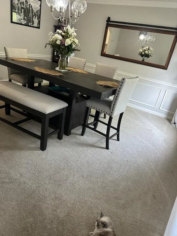 Dining room with dark wood table, upholstered bench and chairs, mirror, and floral centerpiece; small dog on carpet.
