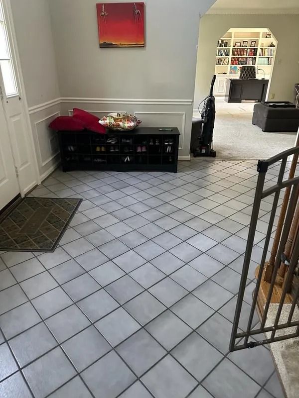 Tiled entryway with black bench, white walls, framed art, and a doorway to a bright room beyond