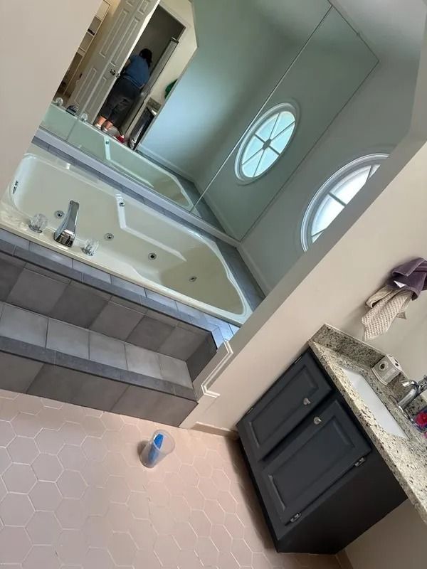 Bathroom with white tub, gray vanity, granite counter, and two round windows; small blue cup on floor.