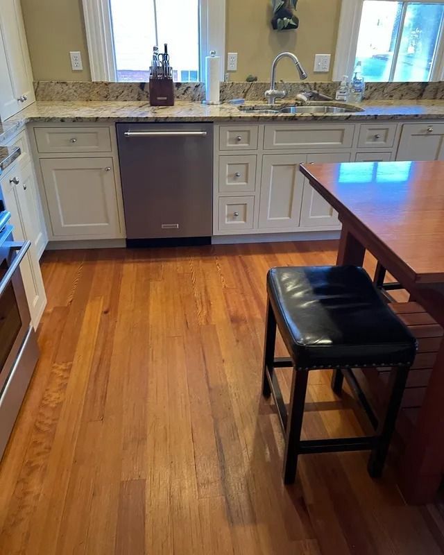 Kitchen with white cabinets, stainless dishwasher, granite island, and a wooden dining table with a black stool.