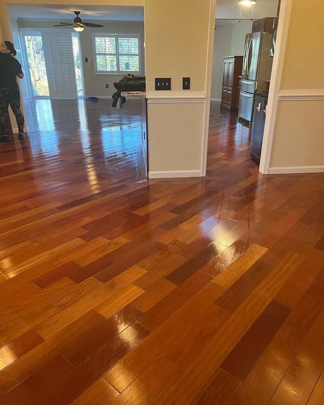 Shiny hardwood living room with open doorways, white walls, and bright windows; two people near the back.