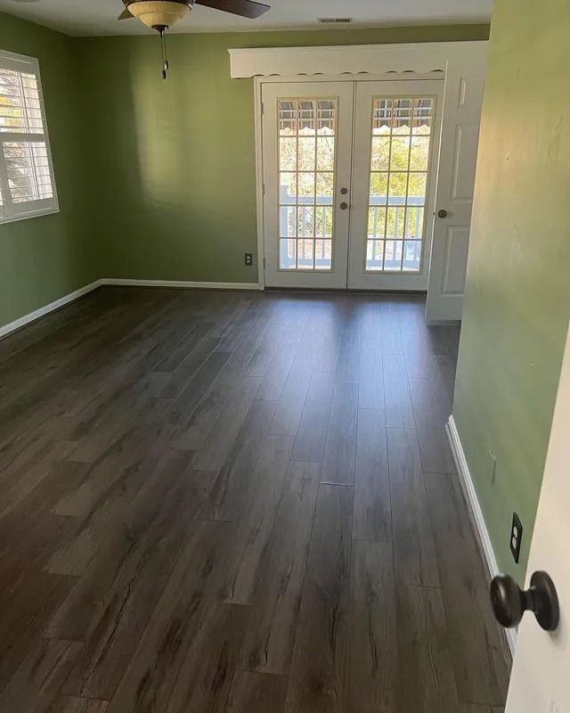 Empty room with green walls, dark wood floor, and French doors opening to a bright exterior