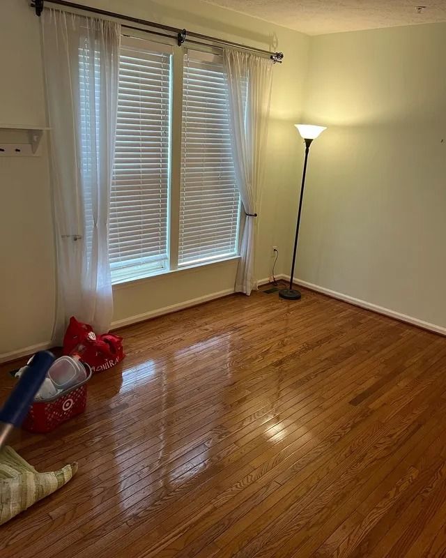 Empty room with hardwood floor, window blinds, floor lamp, and a few cleaning items in the corner