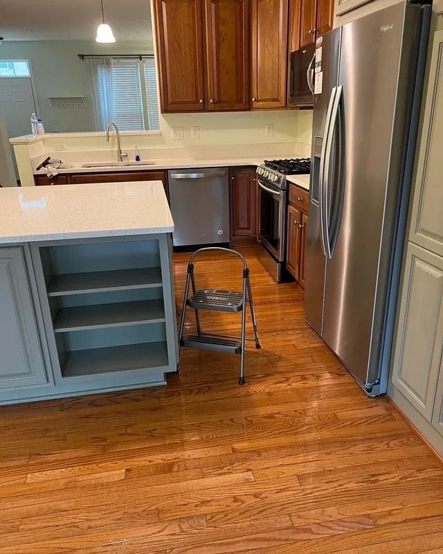 Kitchen with stainless steel appliances, blue cabinets, and a folding chair on a hardwood floor.
