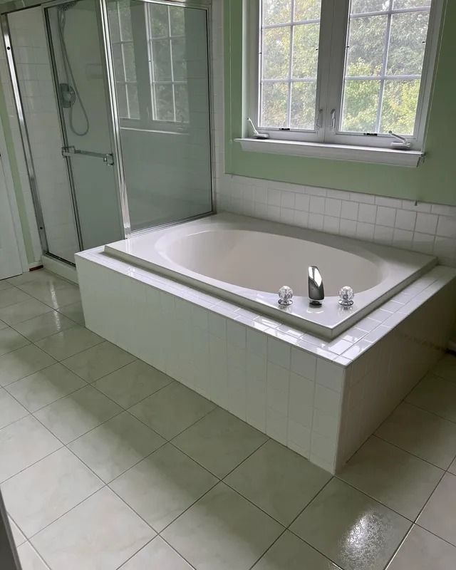 Small tiled bathroom with a built-in white soaking tub, faucet, window, and green walls.
