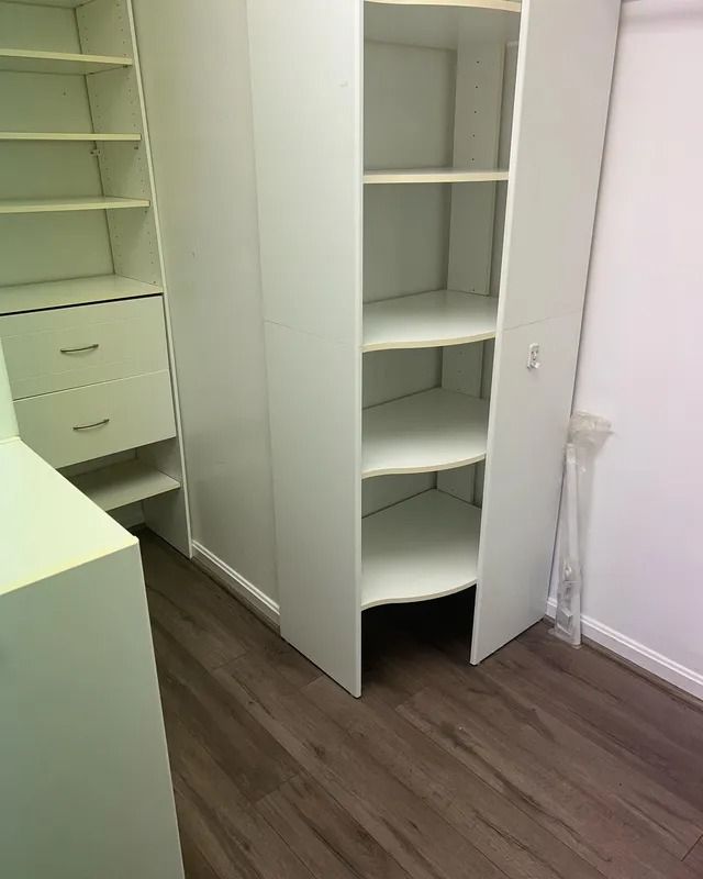 Open closet with white shelves and drawers in a room with dark wood flooring.
