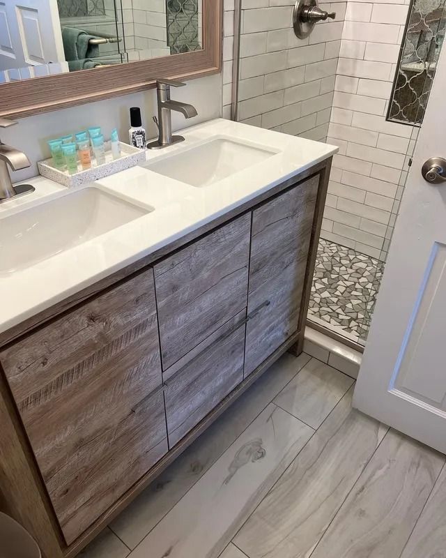 Modern bathroom with double vanity, white sink, wood cabinet, and tiled shower floor