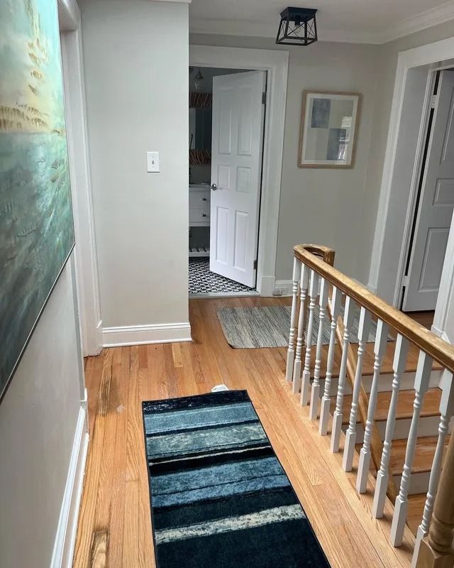 Hallway with hardwood floor, striped runner rug, white doors, and a wooden railing overlooking stairs.