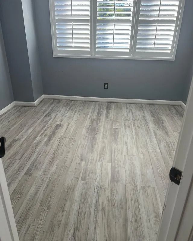 Empty room with gray walls, light wood flooring, and a window with white shutters.