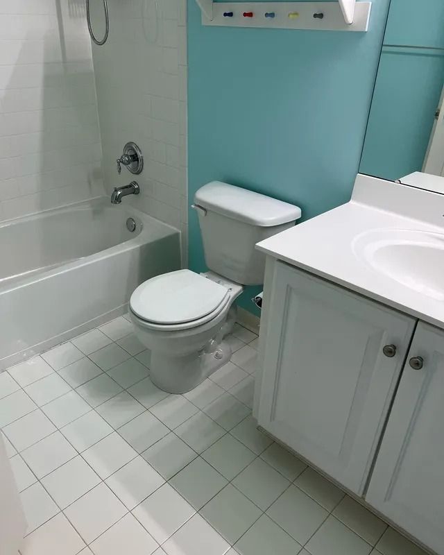 Small bathroom with white toilet, sink cabinet, bathtub, and light blue walls.