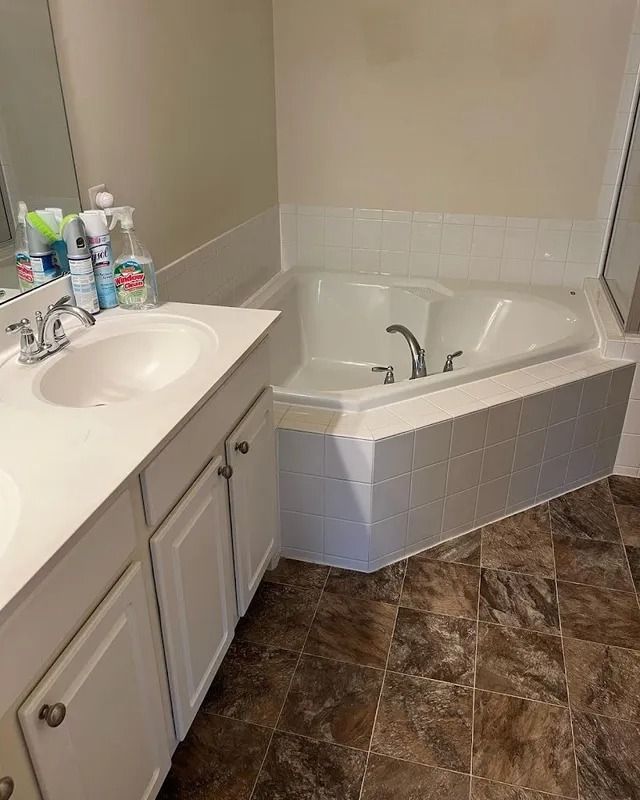 Bathroom with white vanity and corner soaking tub on brown tile floor.