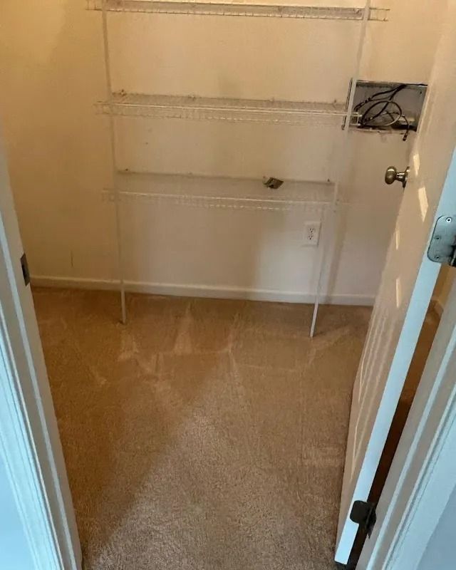 Empty beige closet with wire shelving and carpeted floor, viewed through an open doorway