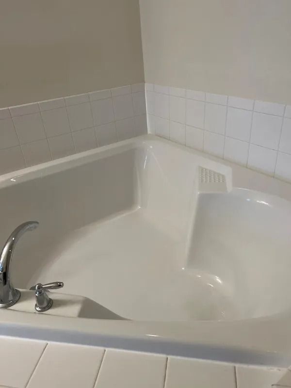 White corner bathtub with chrome faucet in a tiled bathroom