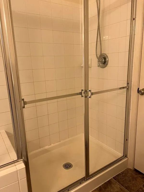 Empty glass-enclosed shower with beige tile walls and a handheld showerhead.