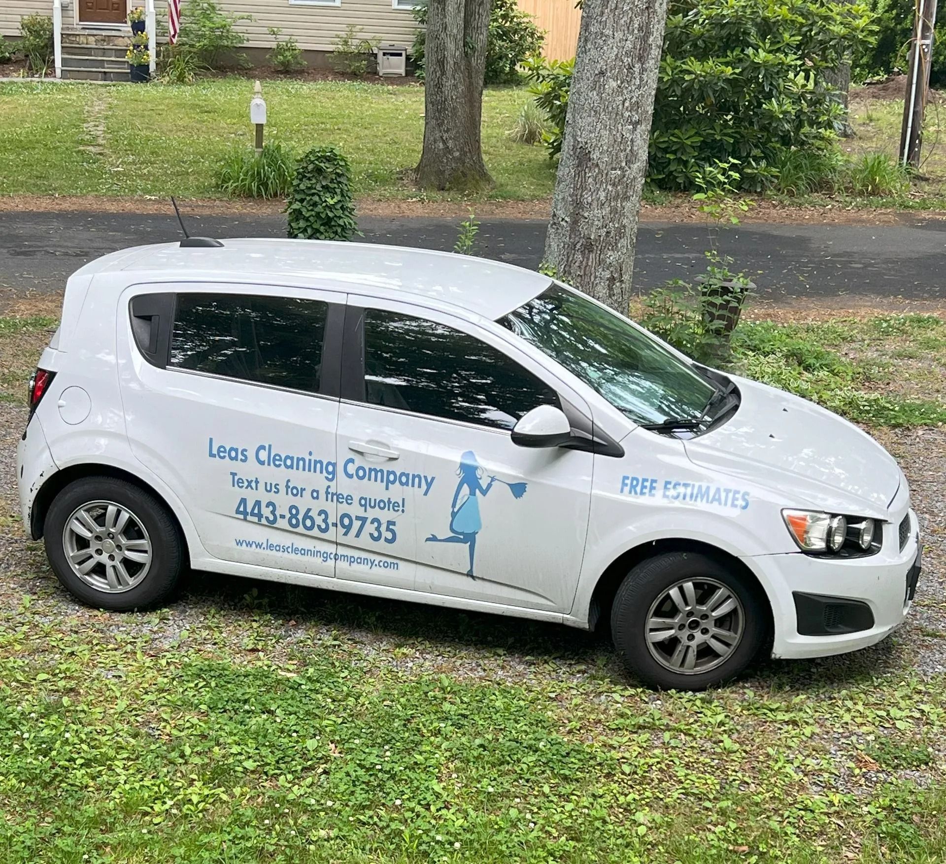 White compact car with “Free Estimates” signage parked on grass in a driveway, side view