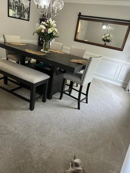 Dining room with dark wood table, bench seating, large mirror, and flowers on the table; small dog at bottom edge.