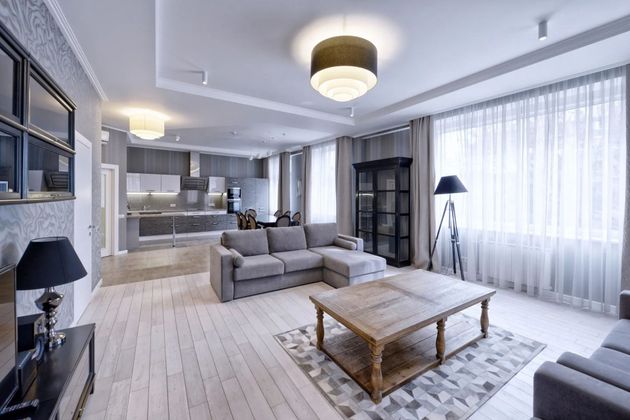 Bright modern living room with gray sofas, wooden coffee table, and large windows with sheer curtains