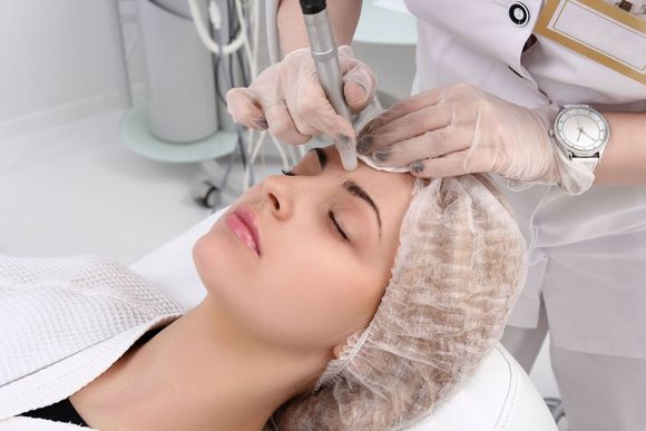 A woman is getting a tattoo on her eyebrows in a beauty salon.