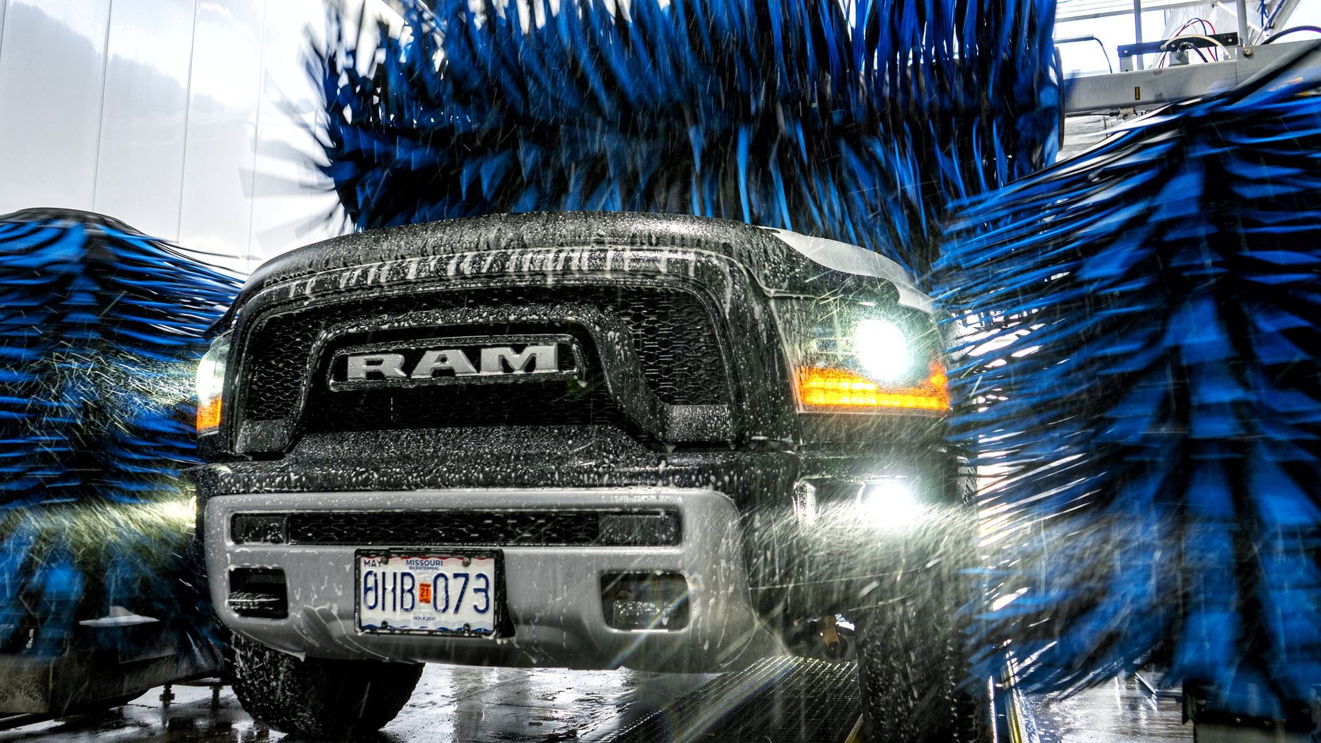 A black RAM pickup truck in a car wash, surrounded by blue brushes and water spray.