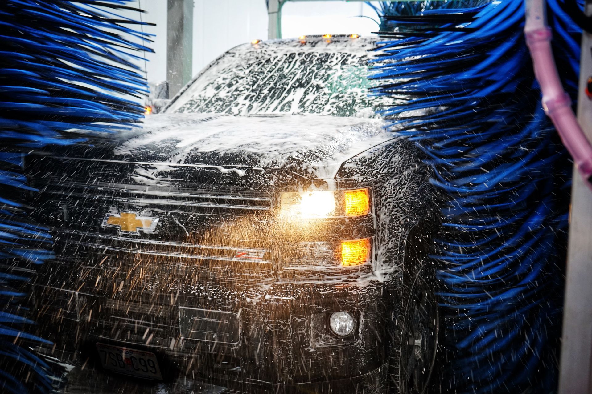 A black Chevrolet truck being washed in a car wash, with blue brushes and foam.