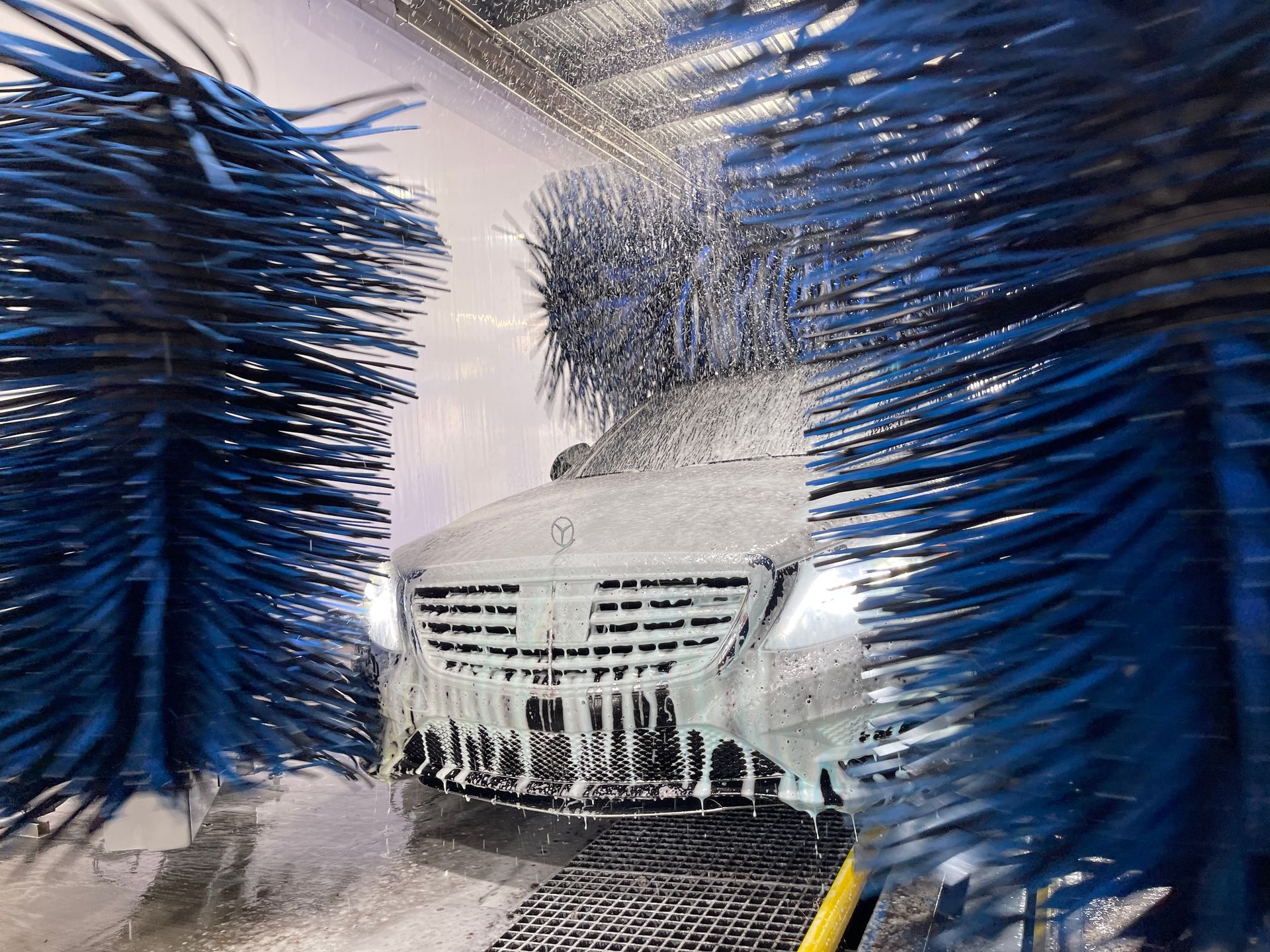 Car being washed in an automated carwash with blue brushes, covered in foam.