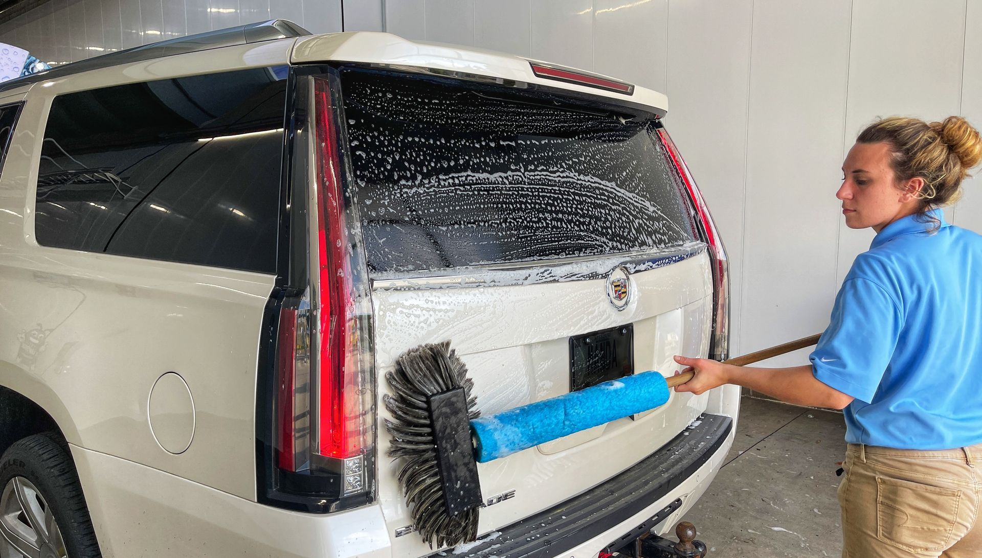 Woman washing a white SUV's rear with a brush. She's in a car wash setting.