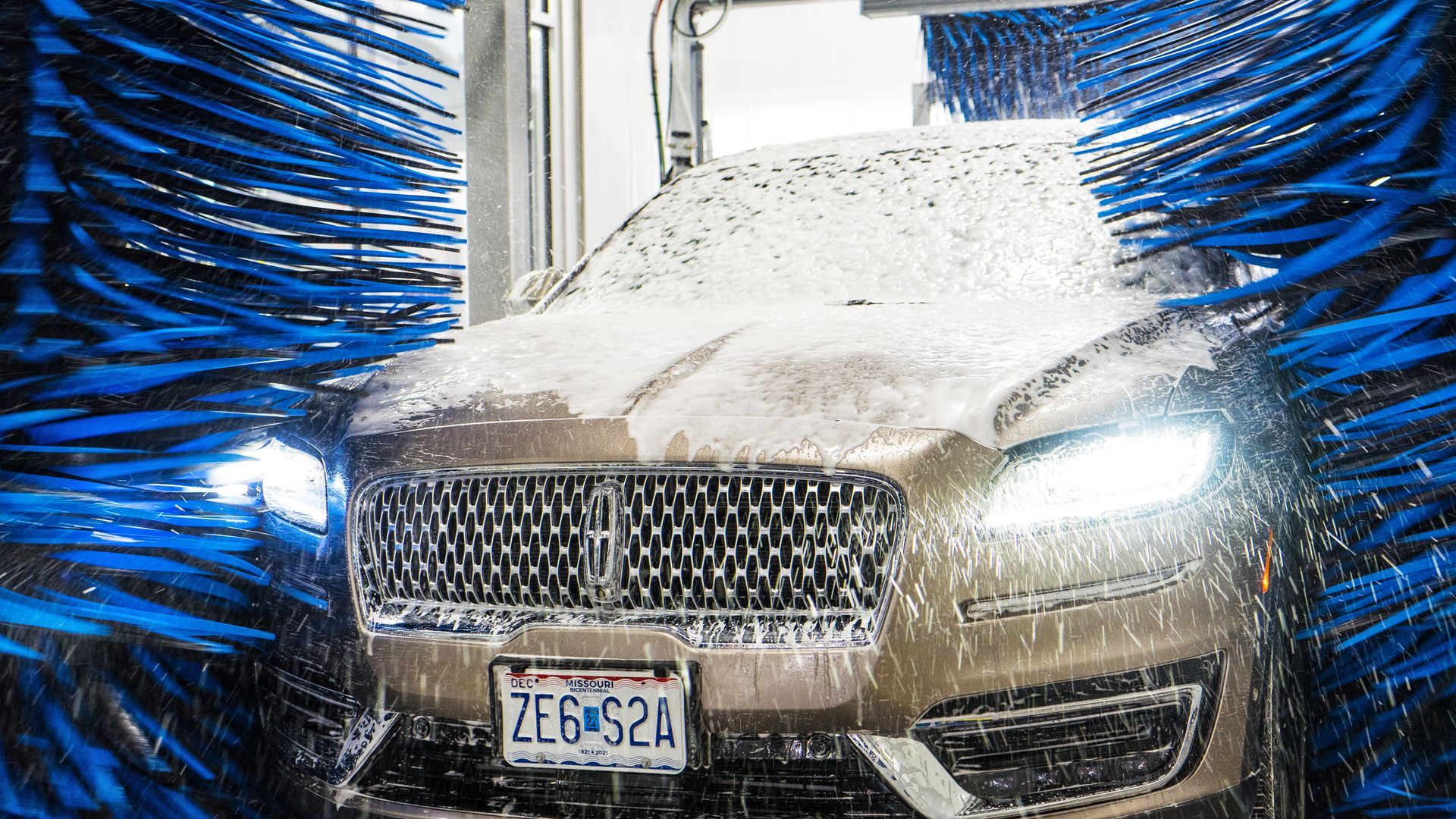Car in car wash, covered in soap, surrounded by blue brushes.