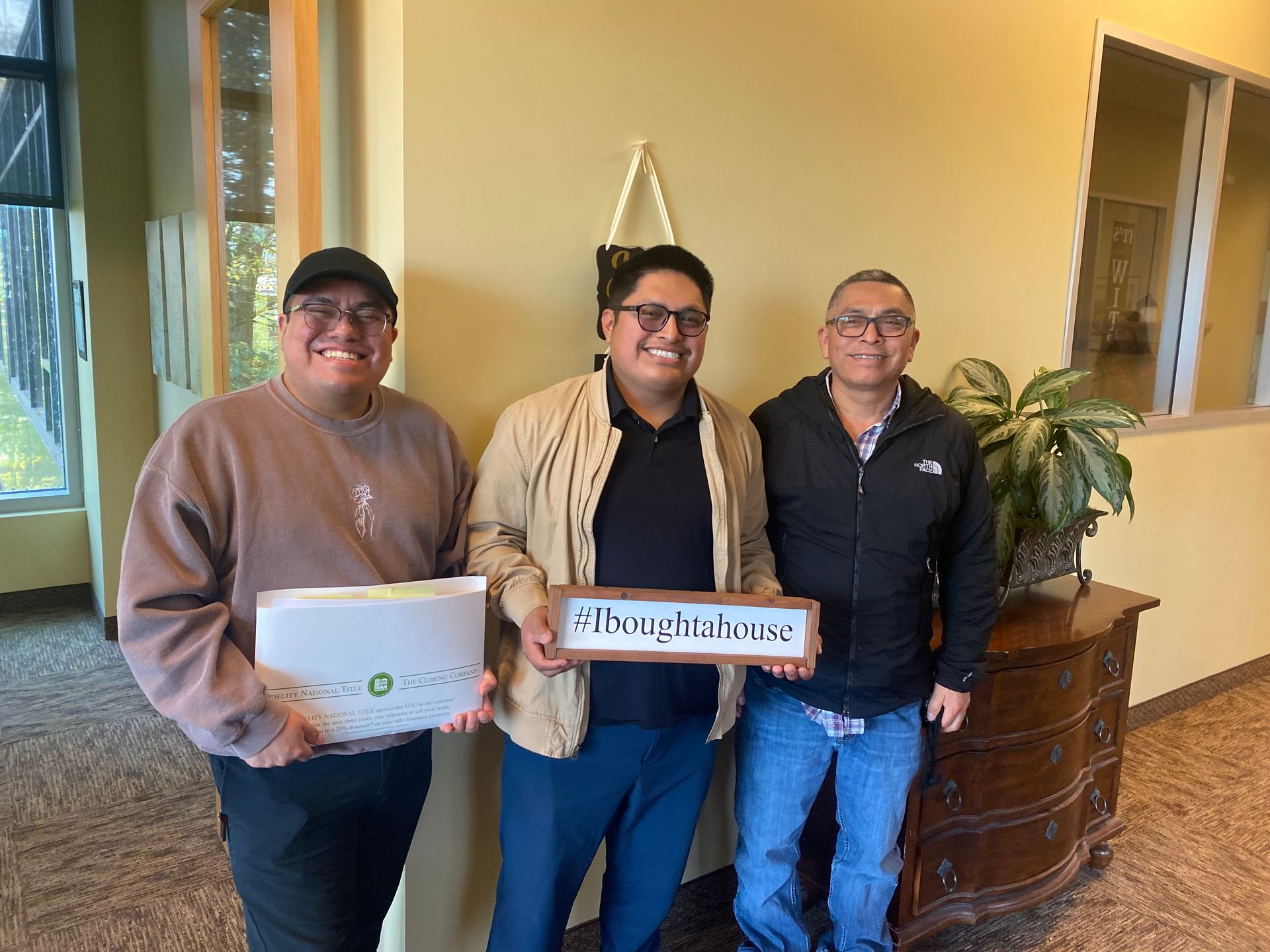 Three men are standing next to each other in a room holding a sign.