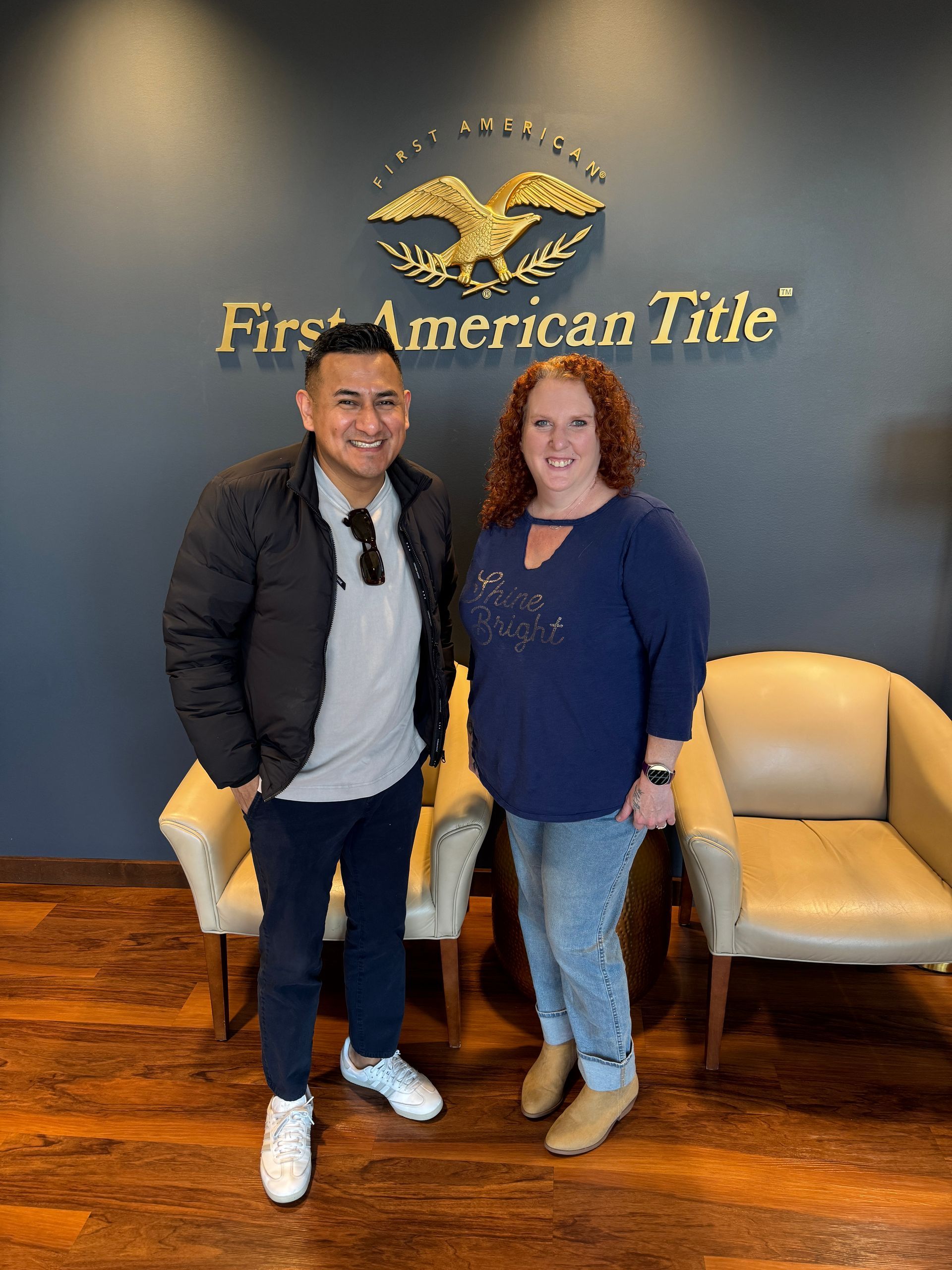 Two people standing in an office lobby with a First American Title sign on the wall.