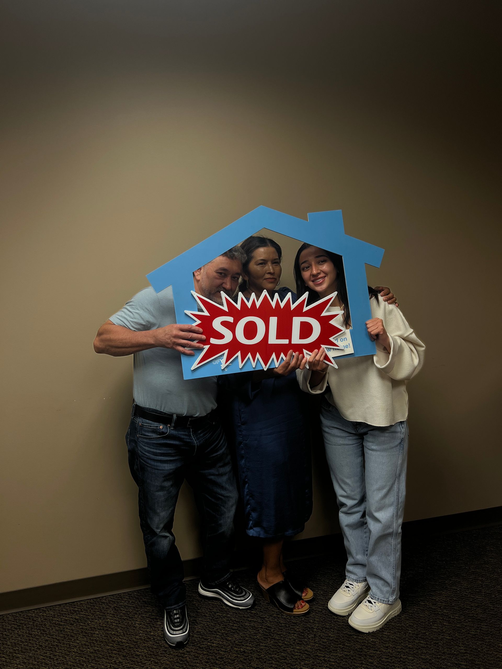 A man and two women are holding a sold sign in front of a house.