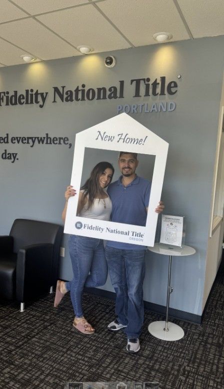 A man and a woman holding a picture frame in front of a wall that says Fidelity National Title.