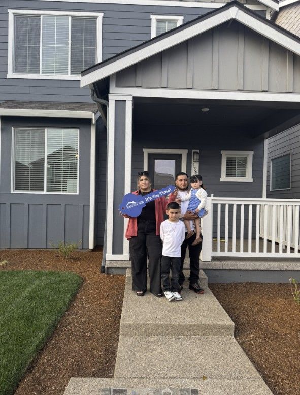 A family is standing in front of a house holding keys.