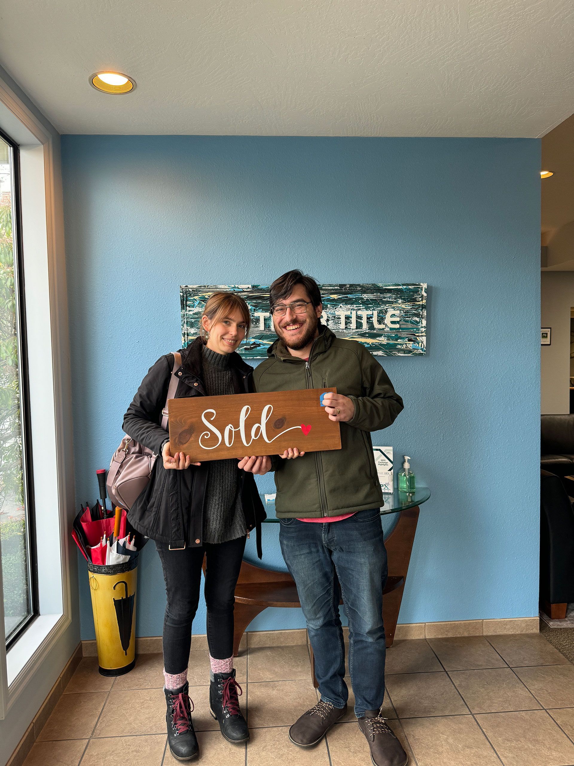 A man and a woman are standing next to each other holding a sold sign